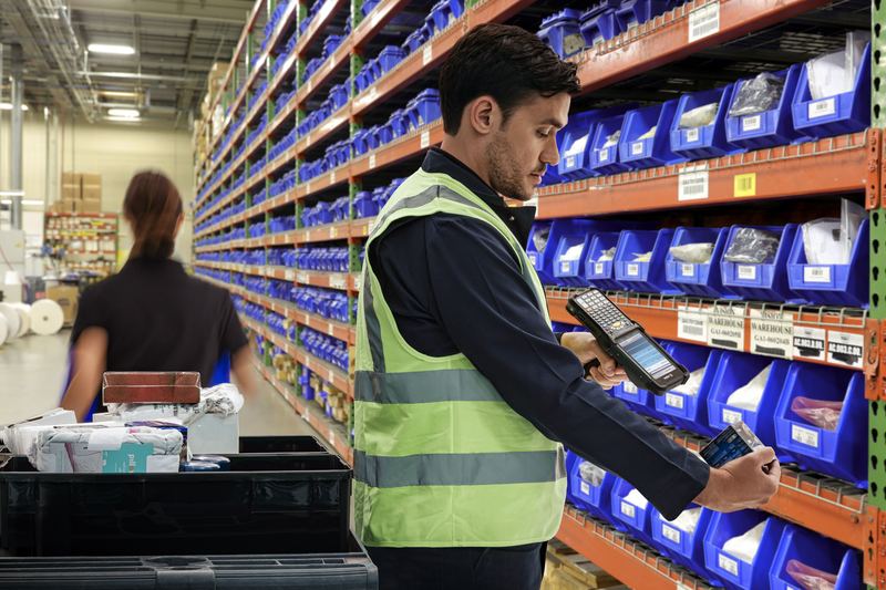 Angajat de depozit scanează marfa de pe raft cu un terminal de colectare a datelor